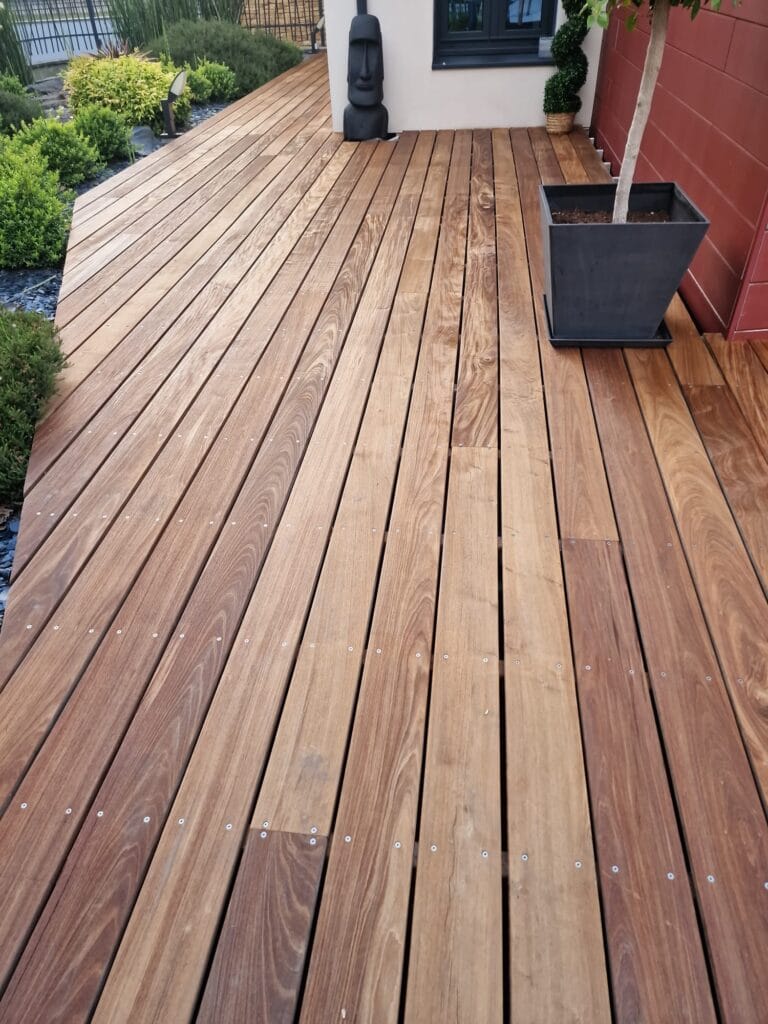 Terrasse en lame de bois devant mur rouge et verdure